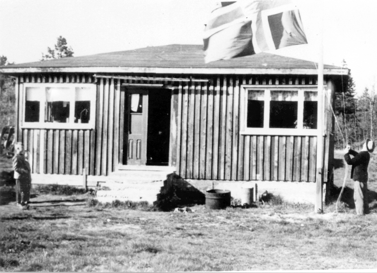 FLAGGHEIS: Jens Bøya heiser flagget utenfor ”bungalowen” ute i Nyhaven. Til venstre står Martin Birkeland og Olav Røstad. Bildet, som er tatt rundt 1960, er utlånt av Birkenes Kameraklubb.
